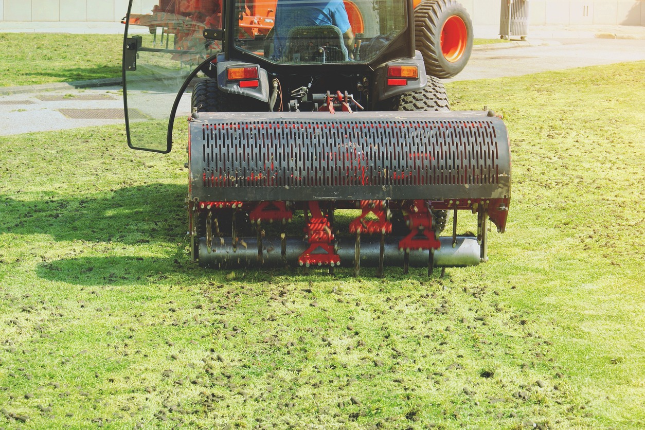 Tractor aerating grass field with lawn aerator attachment