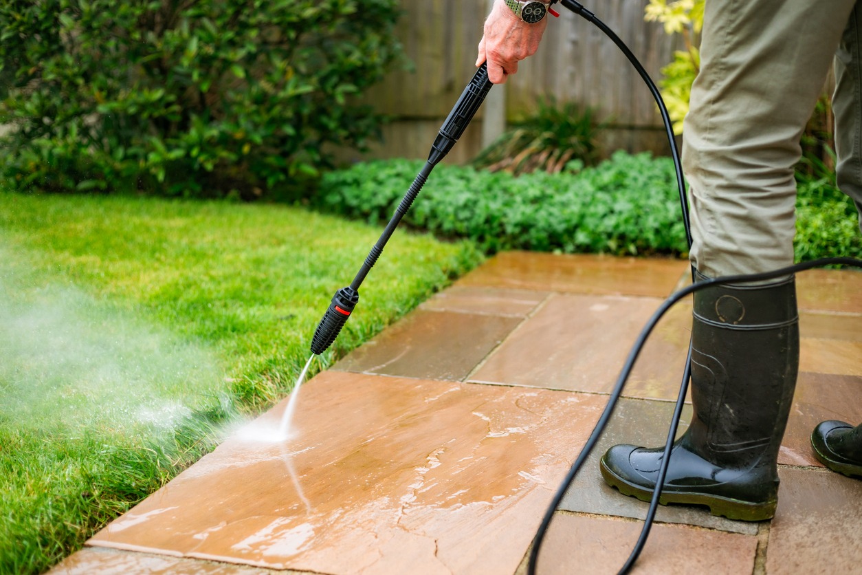 Person pressure washing patio next to lawn