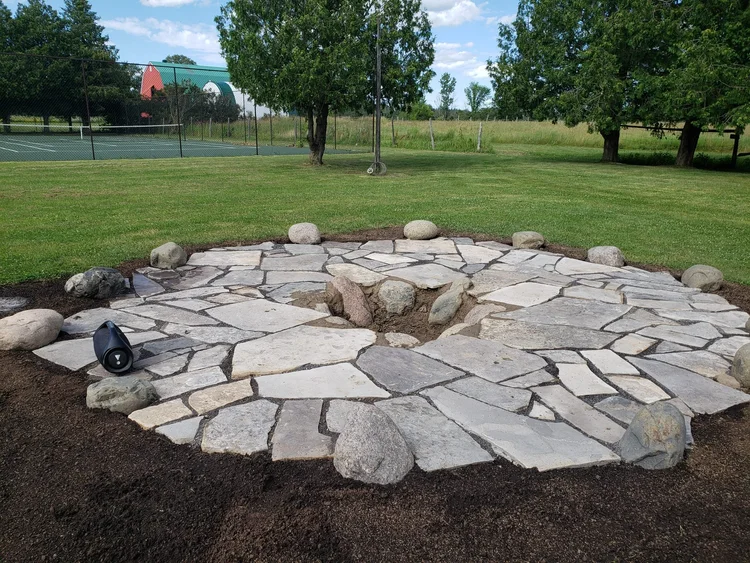 Circular stone patio with rocks in grassy yard