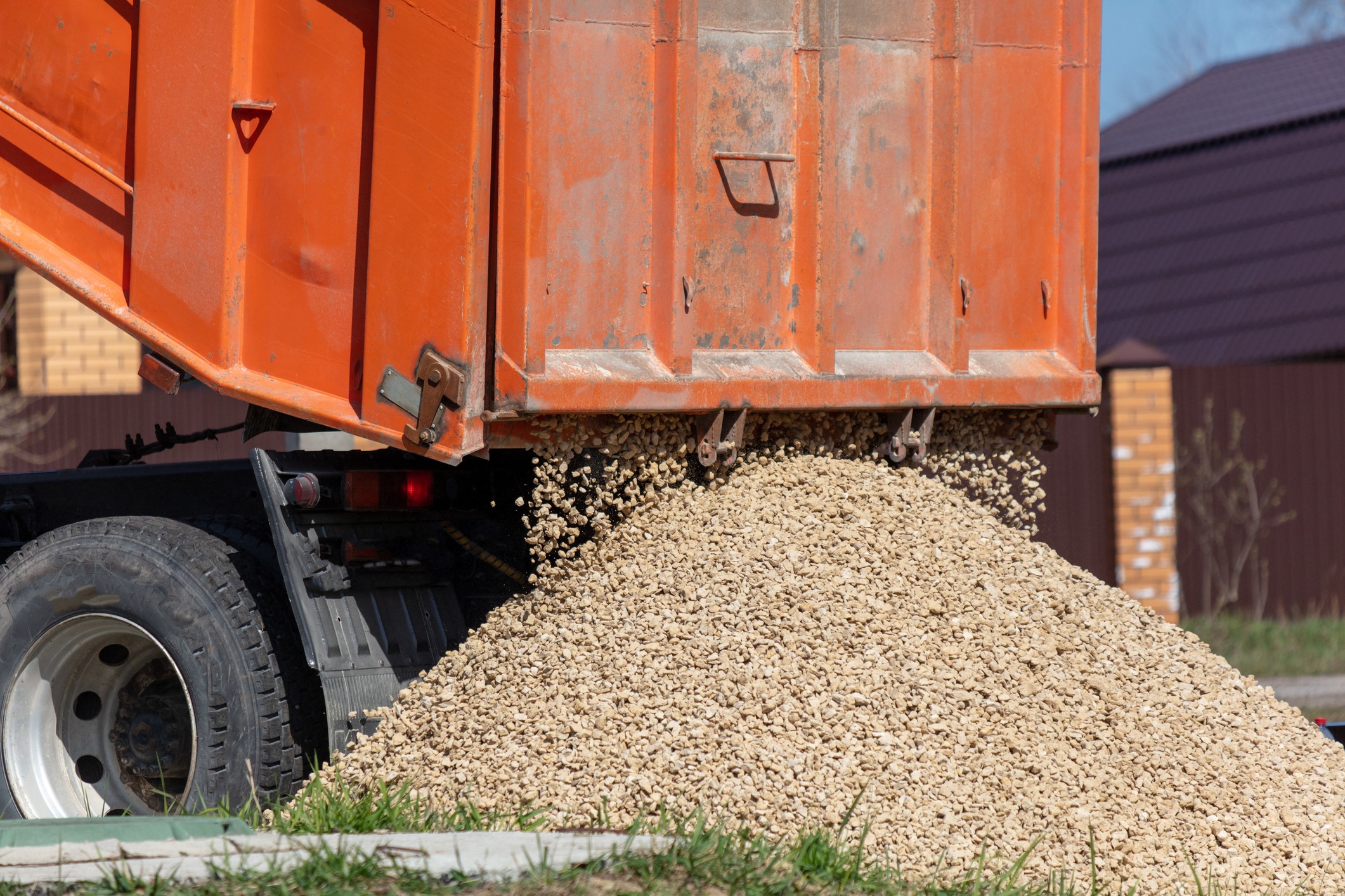Orange dump truck unloading gravel pile