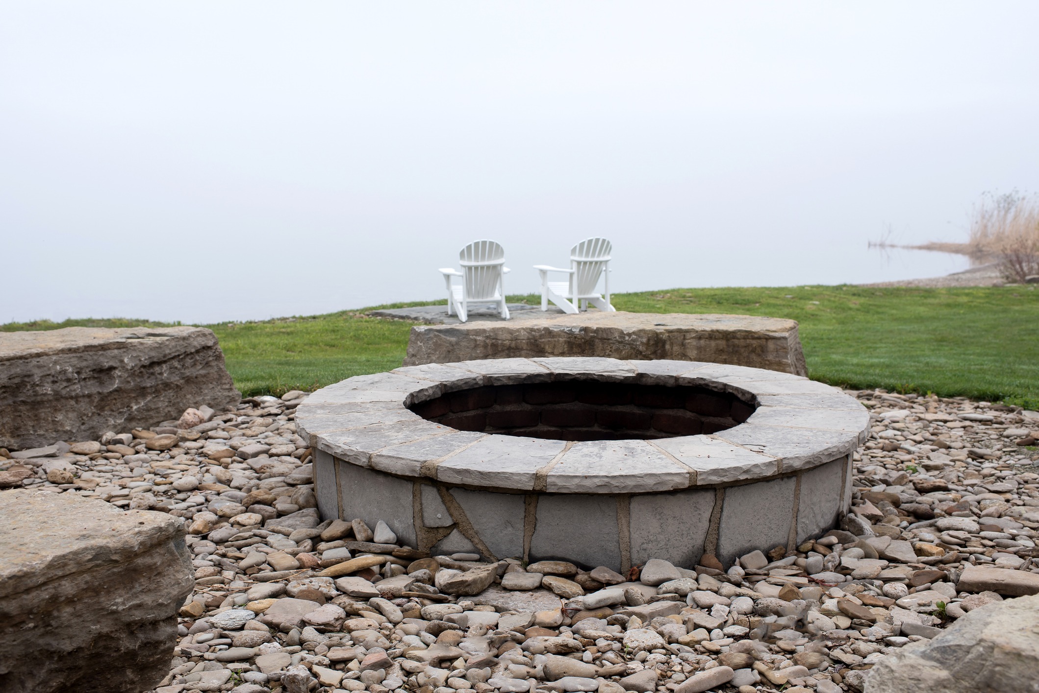 Stone fire pit by foggy lakeside chairs