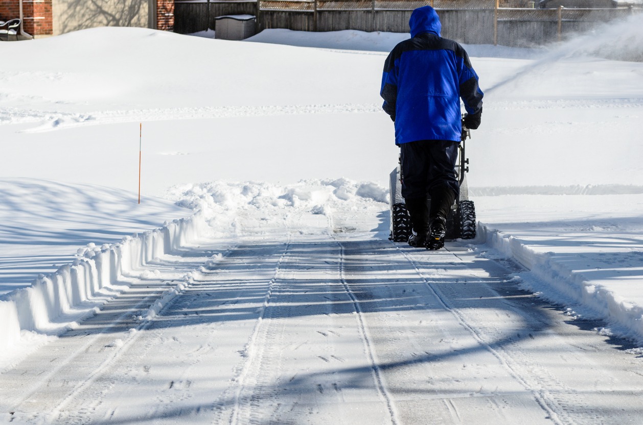 Person using snow blower on snowy driveway